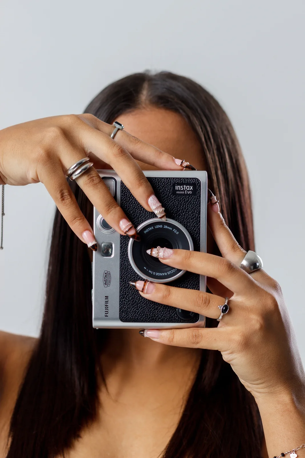 Hands with French tips holding an Instax camera up to the face